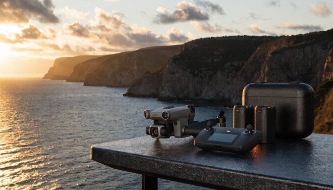 Flagship foldable camera drone with controller, batteries, and carrying case on an outdoor table, highlighting a triple-camera setup for professional aerial video.